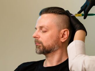 Ein Mann sitzt mit geschlossenen Augen, während eine medizinische Fachkraft mit Handschuhen eine Injektion in die Kopfhaut setzt.