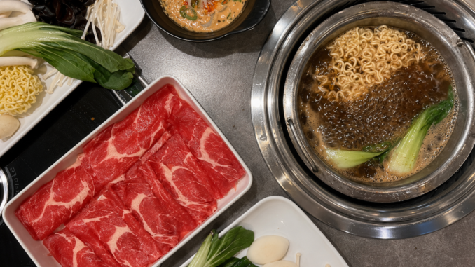 Hot Pot mit würziger Brühe, Nudeln, Pak Choi, dünn geschnittenem Rindfleisch, Pilzen und frischem Gemüse.