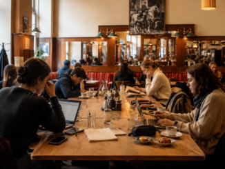 Studierende und Berufstätige arbeiten mit Laptops und Notizbüchern an einem großen Tisch in einem gemütlichen Wiener Café.