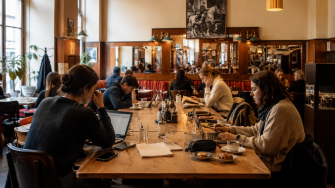 Studierende und Berufstätige arbeiten mit Laptops und Notizbüchern an einem großen Tisch in einem gemütlichen Wiener Café.
