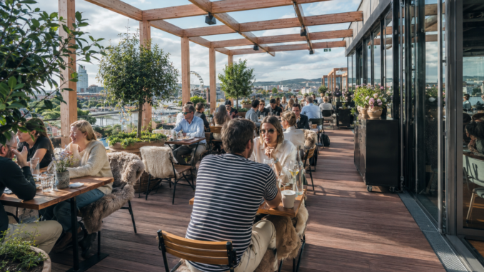 Gut besuchte Rooftop-Terrasse in Wien mit Holzboden, Pflanzen und Blick über die Stadt.