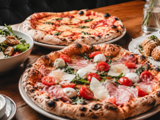 Frisch gebackene Pizzen, Salat und Beilagen auf einem gedeckten Holztisch in einem Restaurant