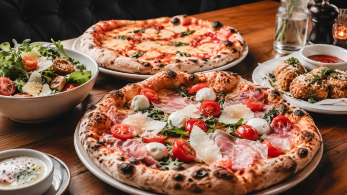 Frisch gebackene Pizzen, Salat und Beilagen auf einem gedeckten Holztisch in einem Restaurant