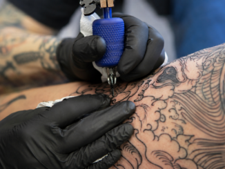 Tattoo-Artist tätowiert mit einer Tätowiermaschine ein großflächiges Motiv auf die Haut einer Person.