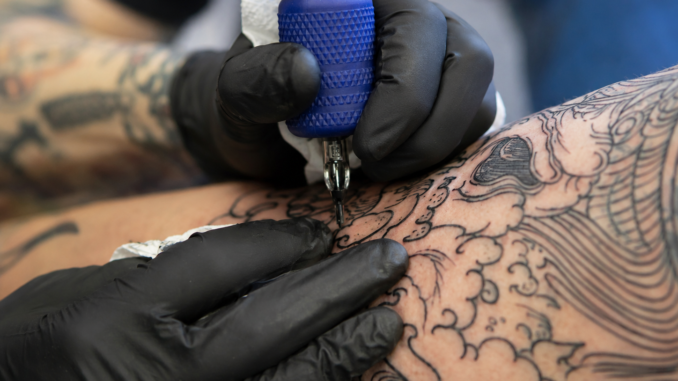 Tattoo-Artist tätowiert mit einer Tätowiermaschine ein großflächiges Motiv auf die Haut einer Person.