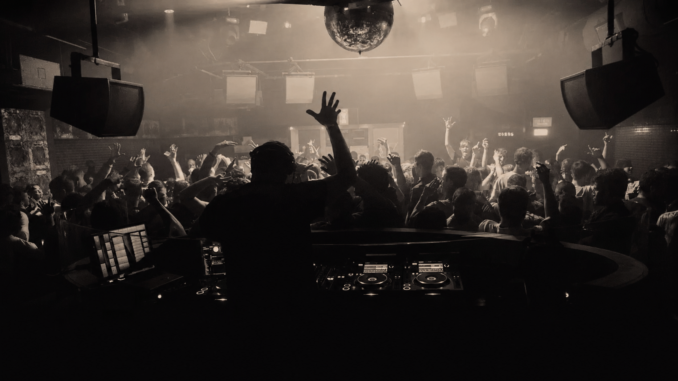 DJ spielt vor einer feiernden Menschenmenge in einem Techno-Club in Wien unter einer Discokugel.